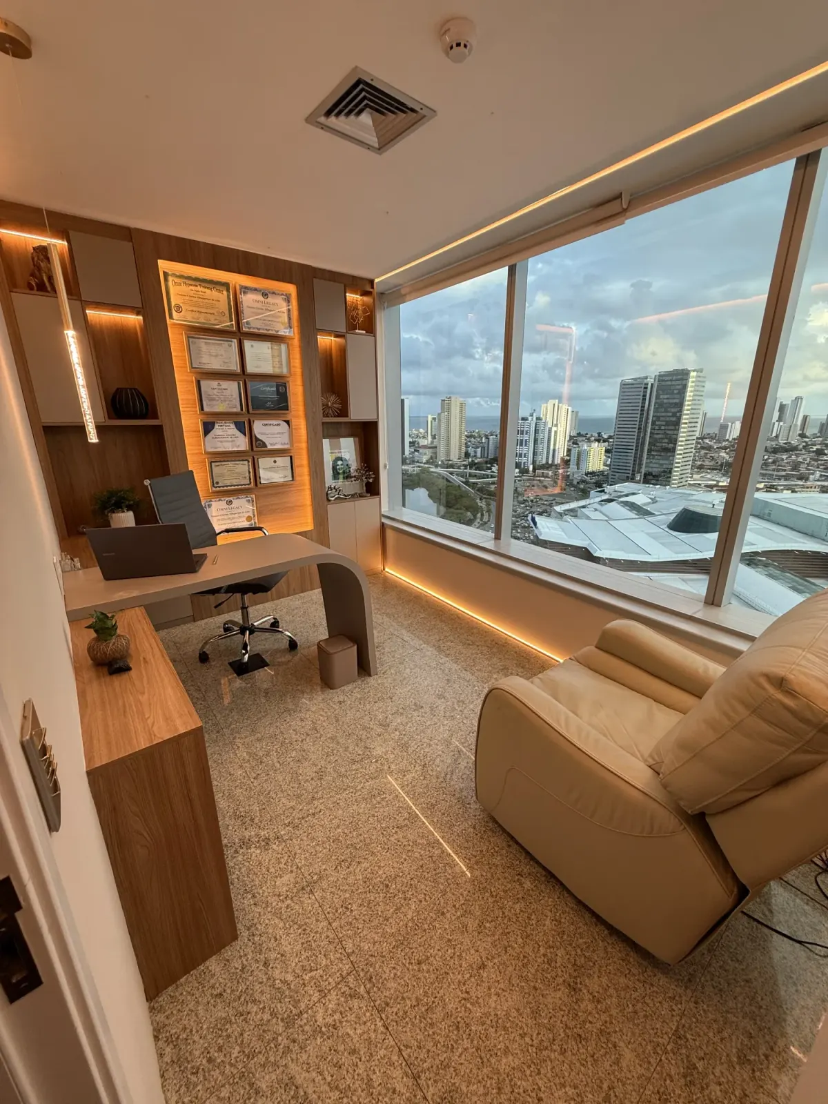 Sala de atendimento da VCare Essence com janela ampla e vista da cidade ao entardecer, poltrona reclinável e luz quente